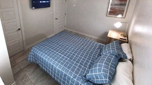 Ein Schlafzimmer mit Bett, Deckenventilator, Wand-Fernseher und Nachttisch mit Lampe.