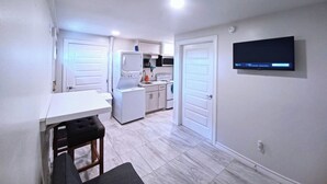 Eine moderne Küche mit weißen Geräten, ein Essbereich mit Tisch und Stühlen sowie ein wandmontierter Flachbildfernseher.