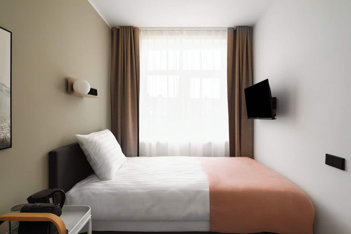 Hotellihuone, jossa on sänky, työpöytä, tuoli, seinälle asennettu taulutelevisio ja ikkuna, jossa on verhot.