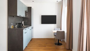 Una cocina moderna con armarios grises, un microondas y una cafetera. Hay una zona de comedor con una mesa y dos sillas. Un televisor de pantalla plana está montado en la pared.