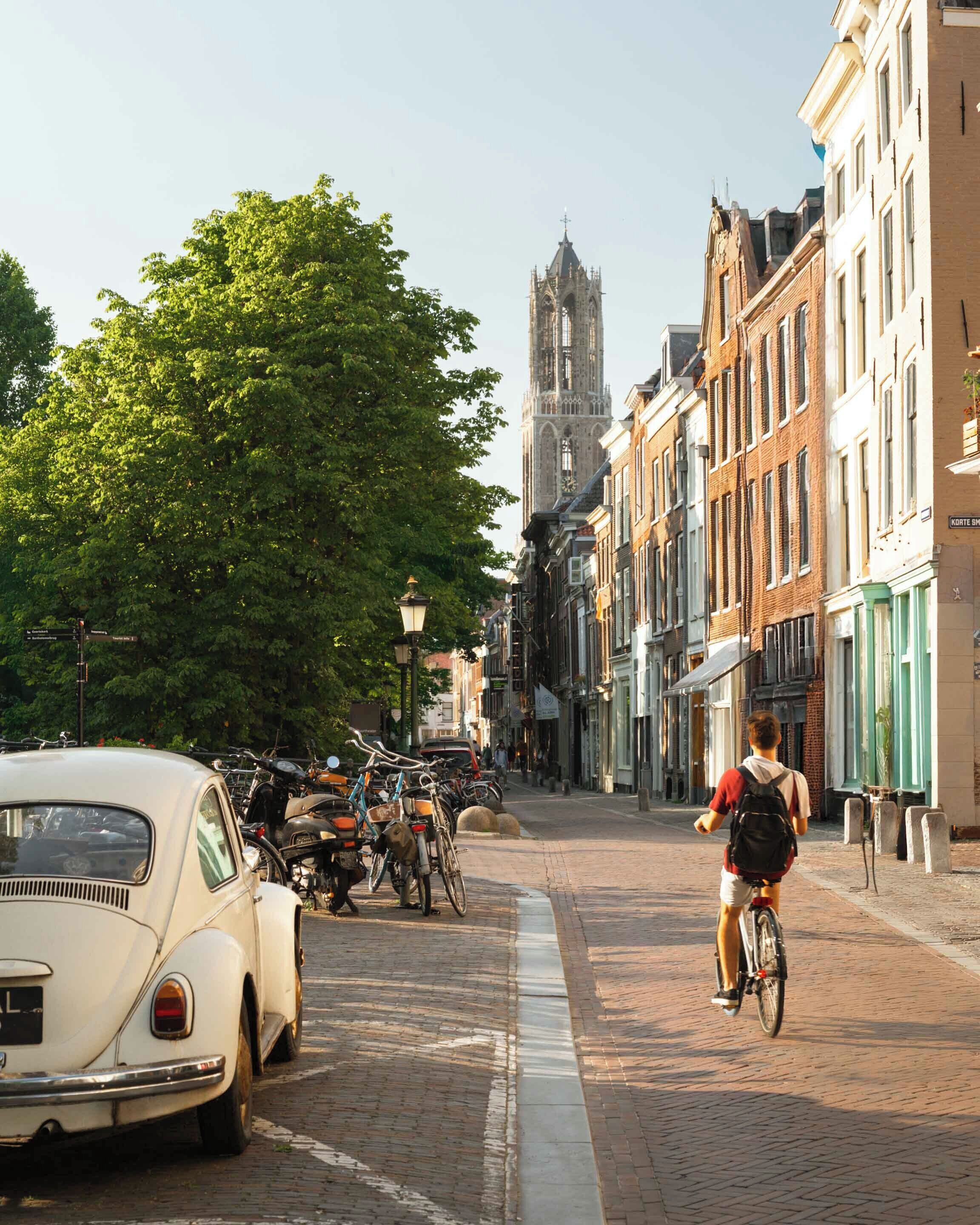 A cobblestone street lined with historic buildings, a vintage car, and a cyclist.