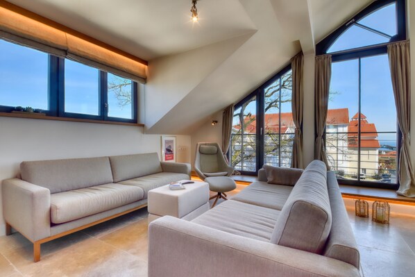 A spacious living room with a large window, a sofa, a chair, and a small table. - Luxury Penthouse 7 at Villa Martha Binz—Your Retreat on the Baltic Sea Coast (Binz)