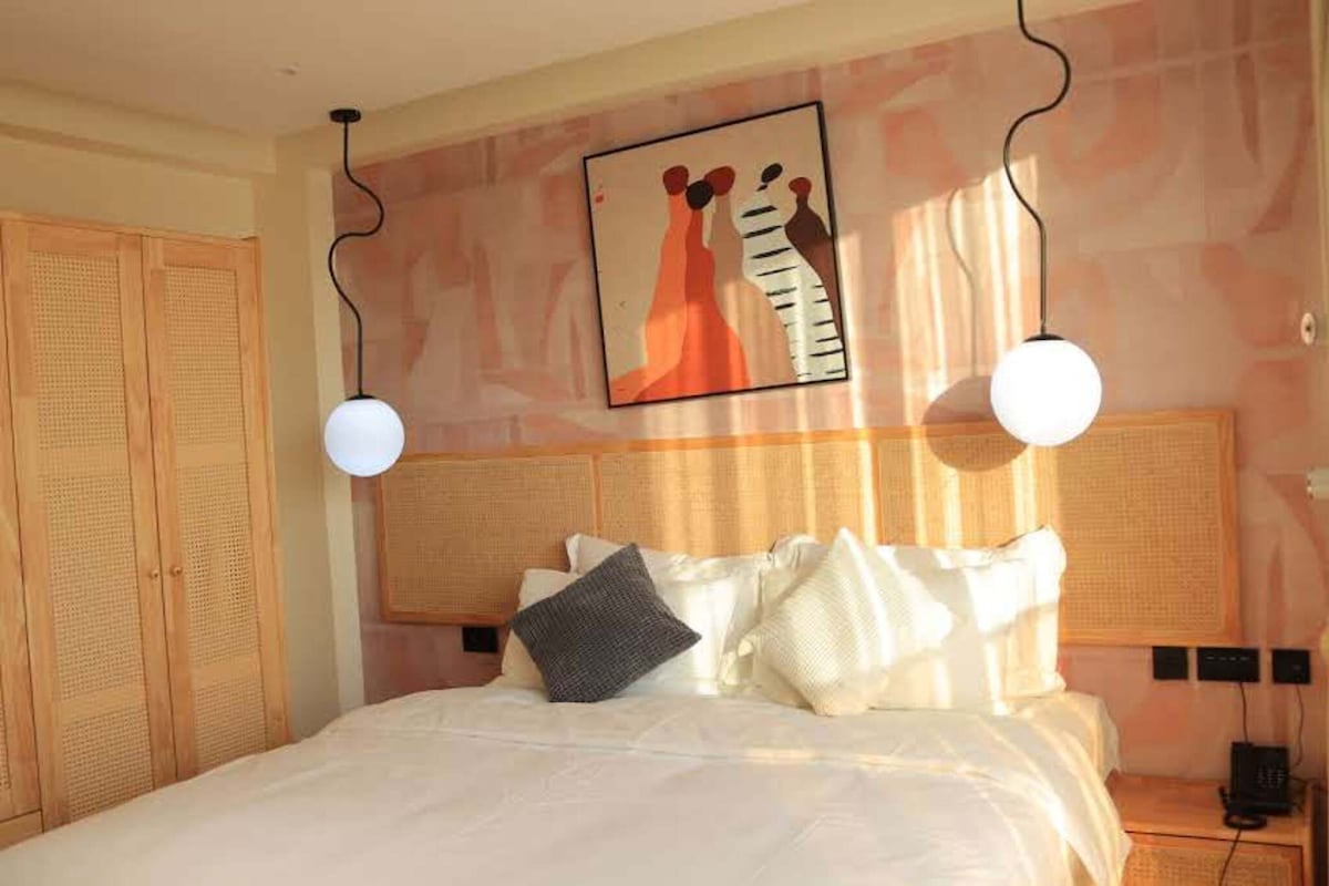 A bedroom with a bed, two bedside lamps, a wall art piece, and a wooden wardrobe.