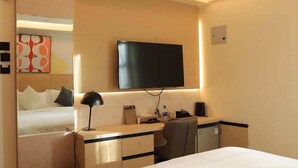 A hotel room with a bed, a desk with a chair, a flat-screen TV mounted on the wall, and a small cabinet. - Arova Hotel (Nairobi)