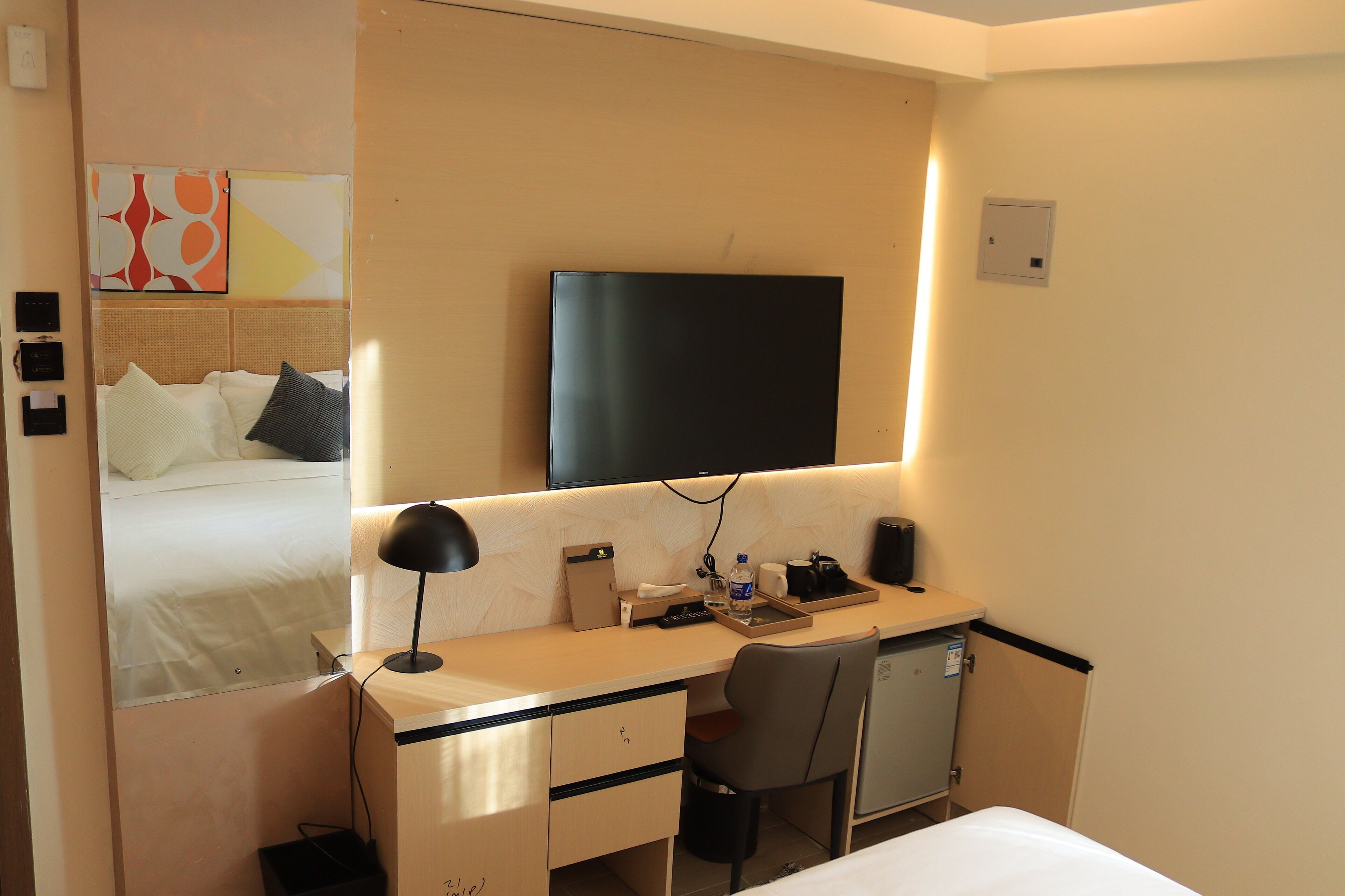 A hotel room with a bed, a desk with a chair, a television, and a small refrigerator.