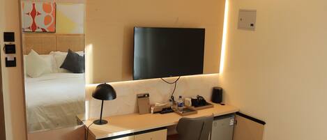 A hotel room with a bed, a desk with a chair, a television, and a small refrigerator.