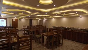 Un comedor amplio con mesas y sillas de madera, suelo de mármol y un diseño de techo moderno con iluminación empotrada.