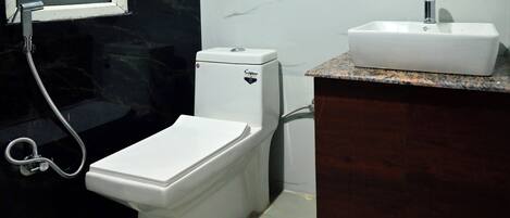 A bathroom with a white toilet, a sink with a marble countertop, and a shower with a black wall.