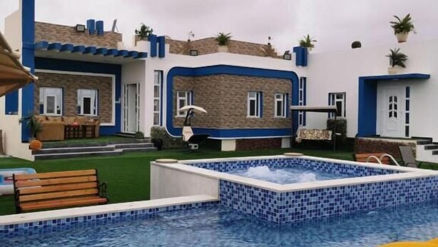 A swimming pool with blue mosaic tiles, surrounded by a building with a blue and white color scheme and stone accents. - Red 12 Almasaraat (Salalah)