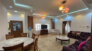 A spacious living room with a round dining table, sofas, and a television. - Red 12 Almasaraat (Salalah)