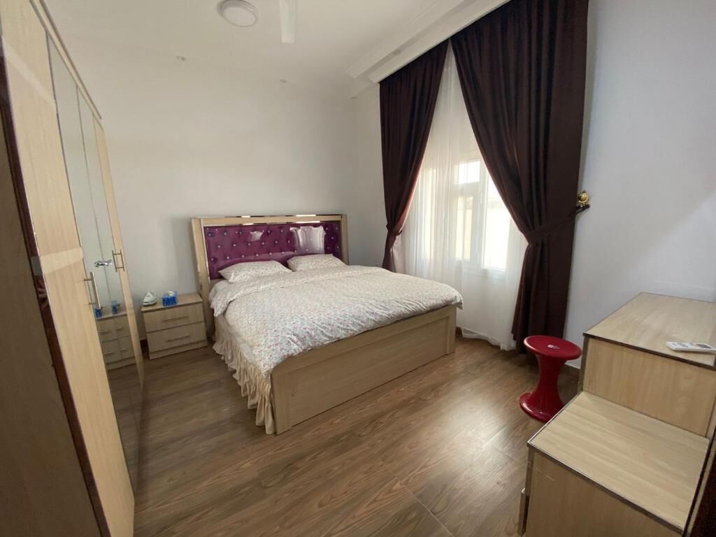 A bedroom with a wooden bed, a red stool, and a wooden desk.
