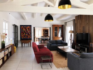 A spacious living room with a high ceiling, a television, and a bookshelf.