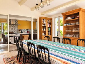 Un espace repas avec une longue table, des chaises, une cuisine en arrière-plan et une bibliothèque remplie de livres et d’objets décoratifs.