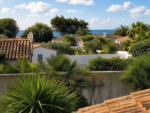 A coastal residential area with terracotta-tiled roofs, lush greenery, and a view of the sea.
