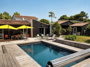 Une piscine avec une terrasse en bois, des sièges d’extérieur et des parasols.