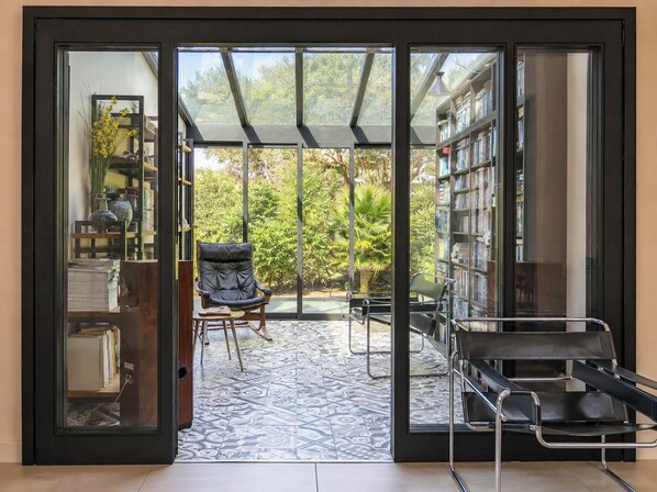 A room with a sliding glass door leading to a patio with a patterned floor, a black leather chair, and a bookshelf filled with books.