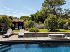 A swimming pool with wooden deck seating and a small house with a tiled roof. - 6-bedroom Villa with pool, 2 min from the sea. Perfect for families (Sainte Marie de Ré)