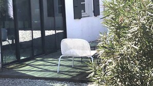 Ein überdachter Patio-Bereich mit einem weißen Stuhl, einer Glastür und einem gefliesten Dach.
