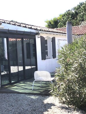 A covered patio area with a white chair, a glass door, and a tiled roof. - 6-bedroom Villa with pool, 2 min from the sea. Perfect for families (Sainte Marie de Ré)