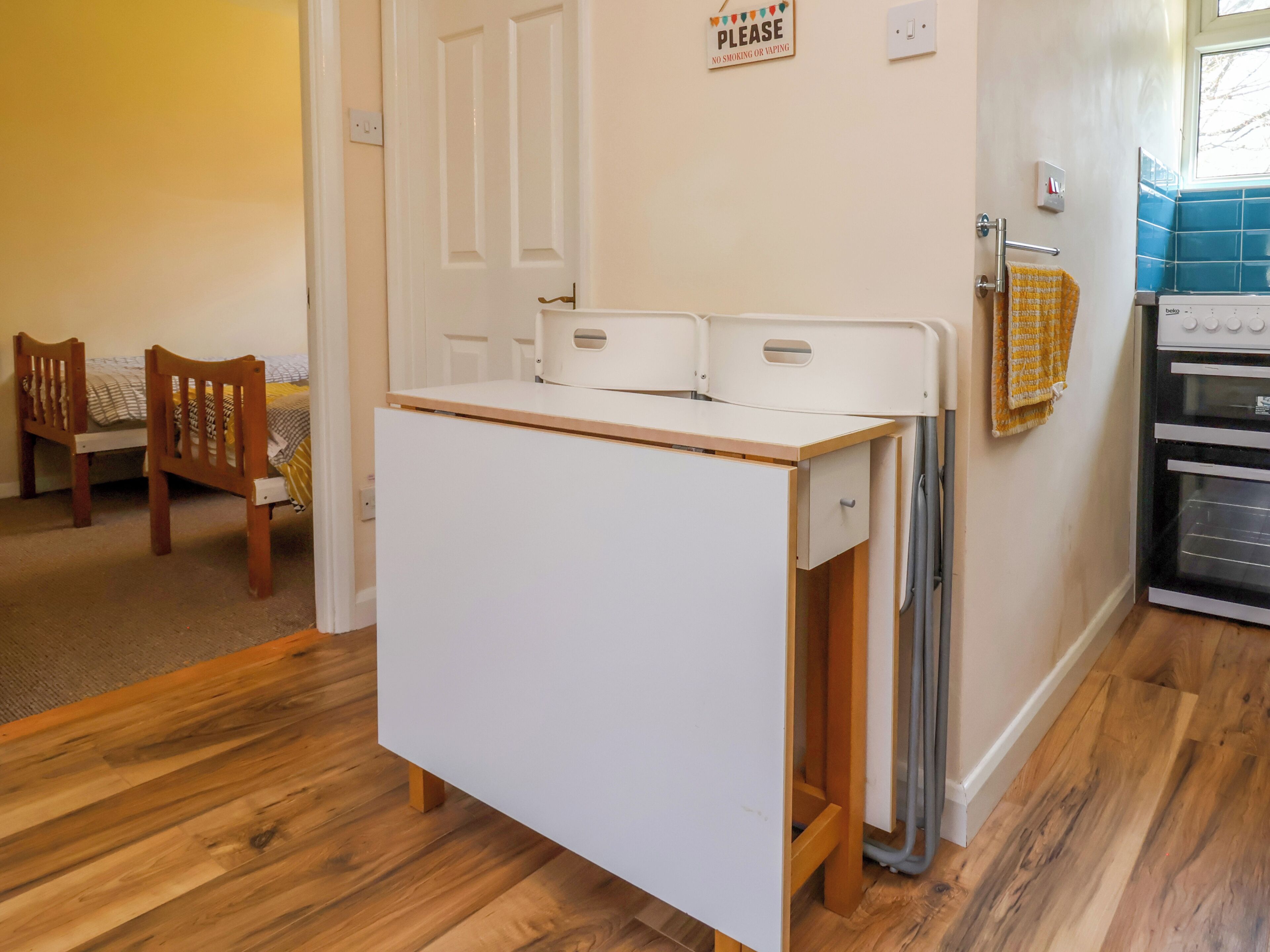 A kitchen with a white countertop, wooden chairs, a small table, and a sign on the wall.