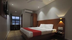 A hotel room with a large bed, a desk with a chair, an air conditioning unit, and a wall-mounted TV.