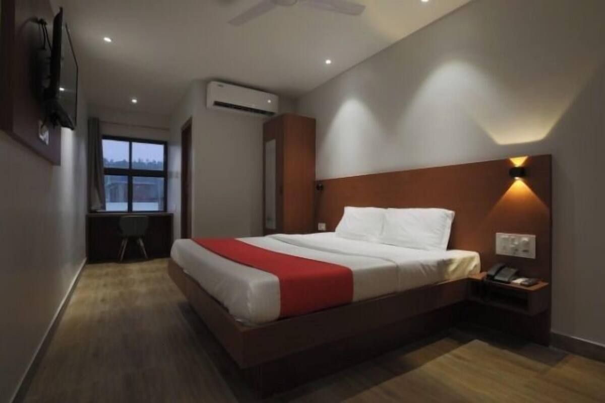 Een hotelkamer met een groot bed, een bureau met een stoel, een airconditioning en een televisie die aan de muur is bevestigd.