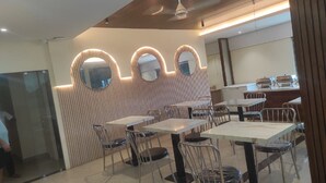 A modern restaurant interior with round tables and chairs, a wooden ceiling, and a wall with three illuminated mirrors.