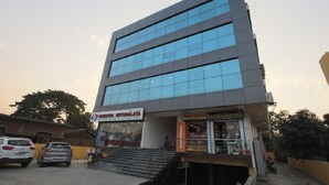 A modern building with a glass facade, a visible ground floor with a sign for 'Trinetria Nethralaya Eye Care Centre' and 'Ma Gahanalaya', and a staircase leading to the entrance.