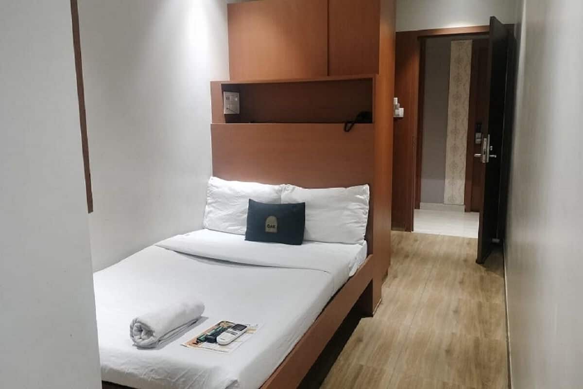 Een hotelkamer met een bed, een houten hoofdbord, een klein plankje en een deur naar een andere kamer.