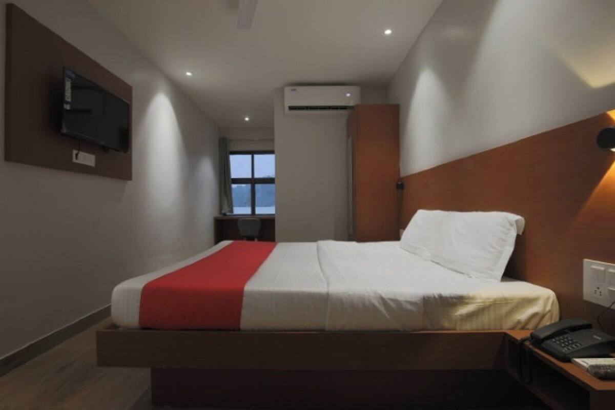Een hotelkamer met een bed, een bureau, een stoel, een aan de muur bevestigde televisie en een airconditioning.