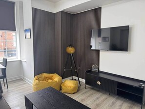 Ein modernes Wohnzimmer mit Flachbildfernseher, Dreibeinlampe und gelbem Sitzsack.