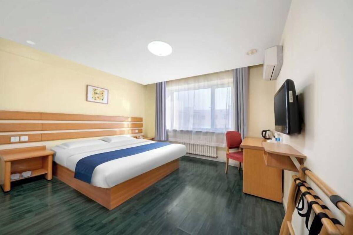 A hotel room with a bed, a desk, a chair, a television, and a window with curtains.