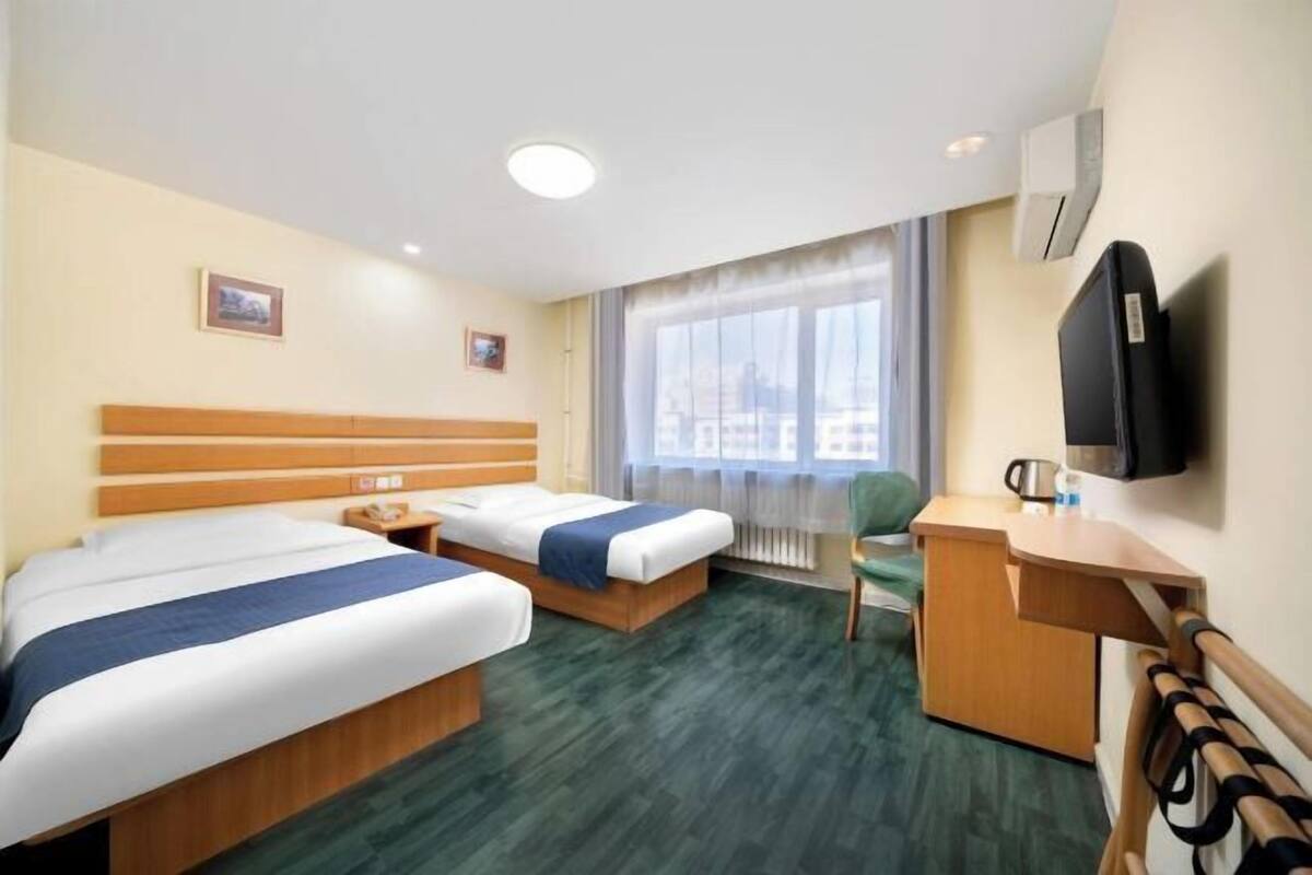 A hotel room with two beds, a desk, a chair, a TV, and a window with curtains.