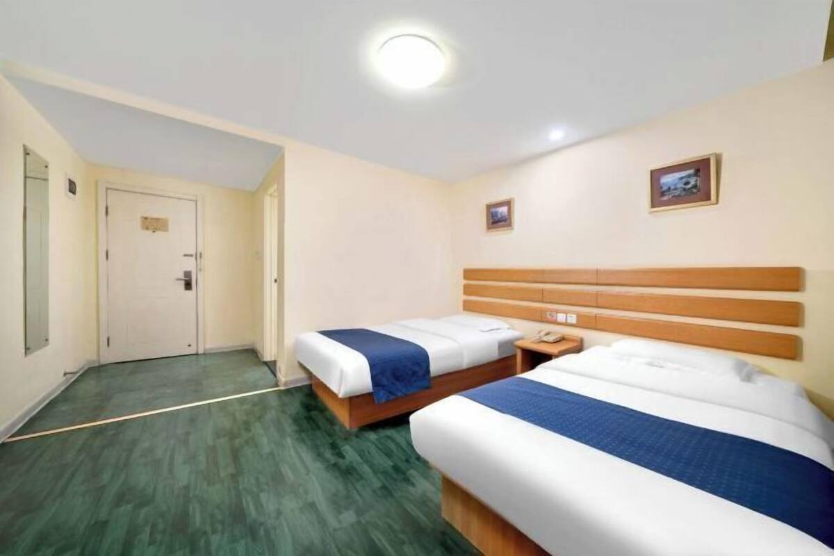 A hotel room with two beds, a wooden headboard, a bedside table with a phone, and a door.