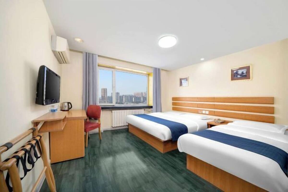 A hotel room with two beds, a desk, a chair, a television, and a window with a city view.