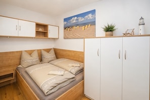 Een slaapkamer met een bed, een houten hoofdbord, een witte kledingkast en een schilderij met een strandthema.