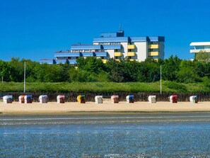 Een gebouw aan de kust met meerdere balkons, een zandstrand op de voorgrond en een helderblauwe lucht.
