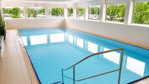 Una piscina interior con baldosas azules y cristalinas, una barandilla metálica y escalones de acceso.