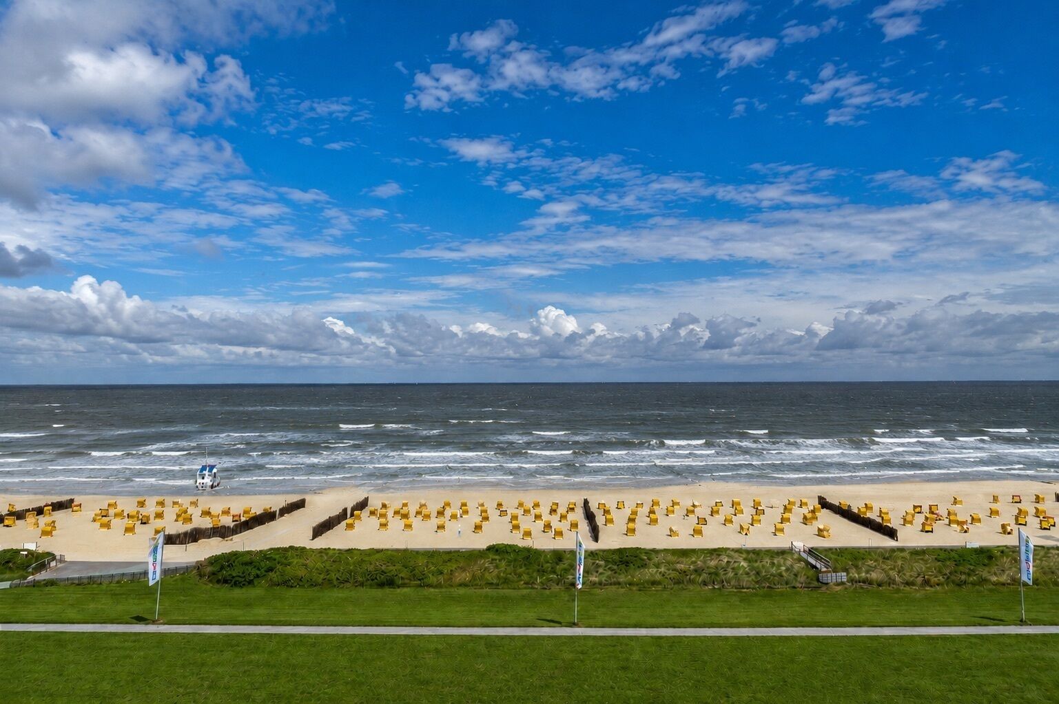 Une plage avec des chaises jaunes disposées en rangées, un poste de surveillance pour les sauveteurs et une vue dégagée sur l’océan.