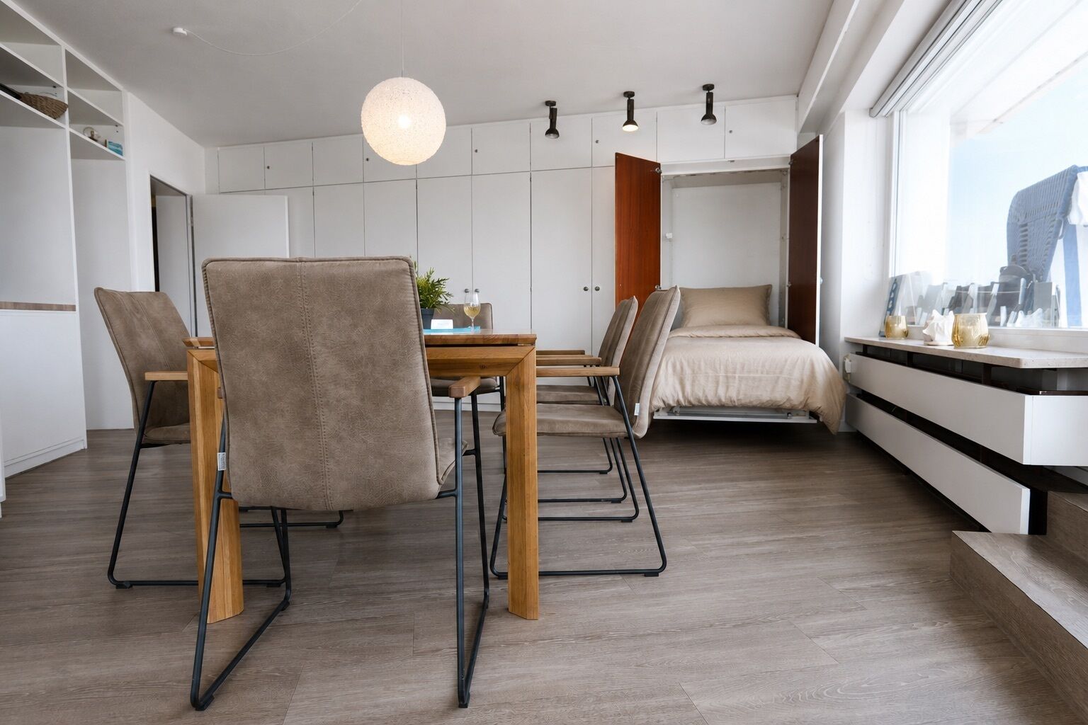 Een moderne kamer met een eettafel, stoelen, een bed en een groot raam.