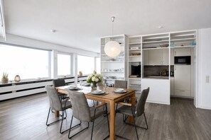 A modern kitchen with white cabinetry, a wooden dining table, and a pendant light. - Luxurious penthouse Duhner Strand with sea view | Haus Hanseatic (Cuxhaven)