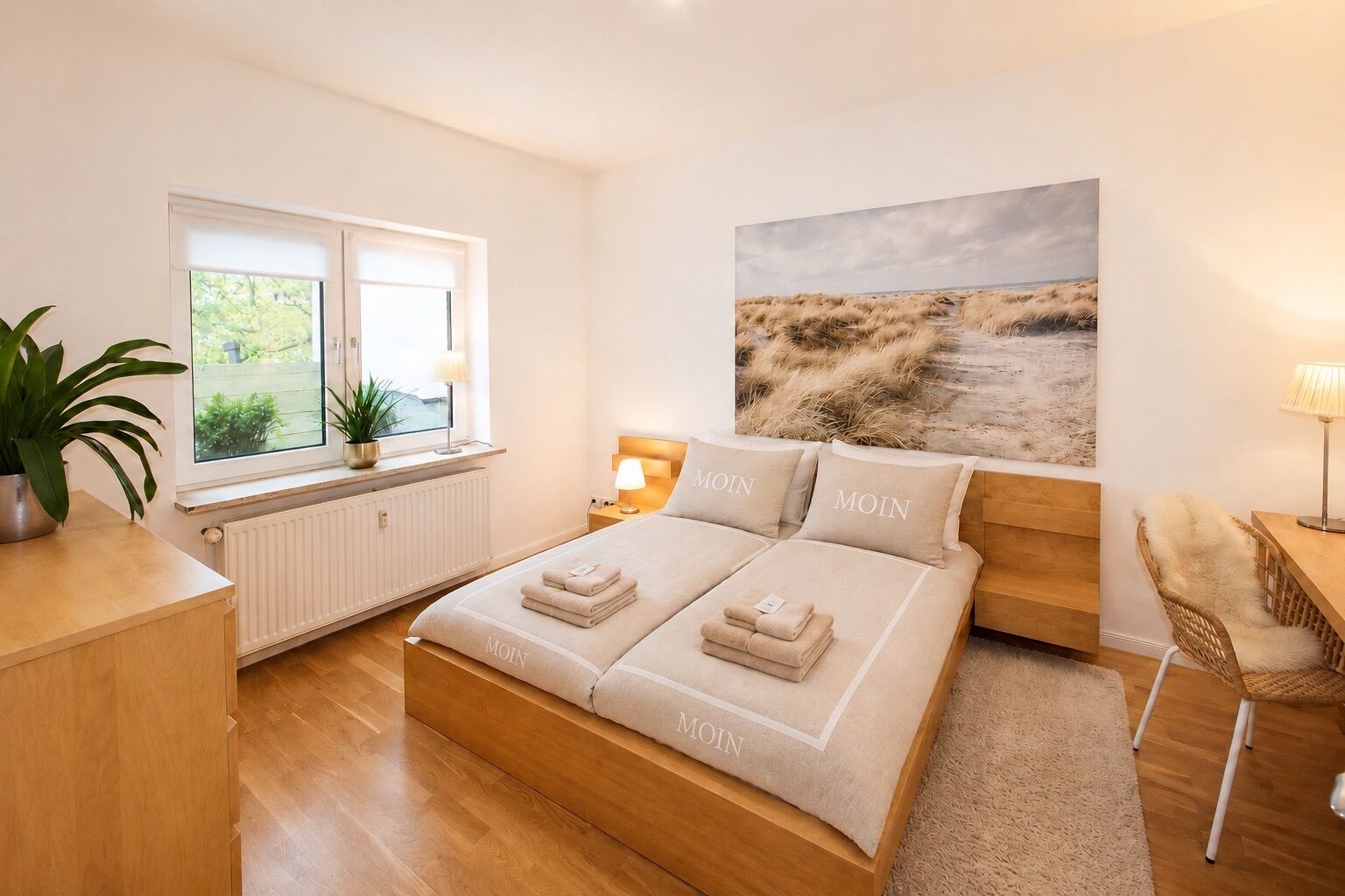 Un dormitorio con cama, mesitas de noche, ventana con vistas, una planta y un cuadro en la pared.
