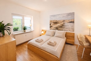 A bedroom with a bed, bedside tables, a window with a view, a plant, and a painting on the wall.