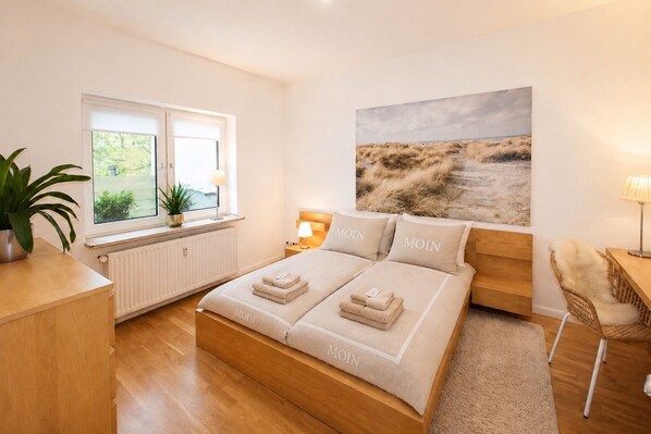 Un dormitorio con cama, mesitas de noche, ventana con vistas, una planta y un cuadro en la pared.