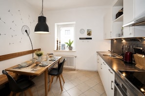 A modern kitchen with a dining area, featuring a black pendant light, a window with a view, and a stainless steel stove.