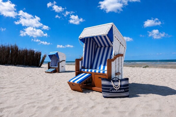 Beach chairs with striped cushions and a beach bag labeled 'Cuxhaven' on a sandy beach.