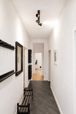 A hallway with a black metal rack, a ceiling-mounted light fixture, and a door leading to a room with a wooden floor.