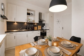 A modern kitchen with white cabinets, a black countertop, and a dining area set for four with plates, glasses, and cutlery.