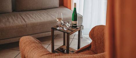 Una sala de estar con un sofá, una mesita con una botella y vasos, y una silla.