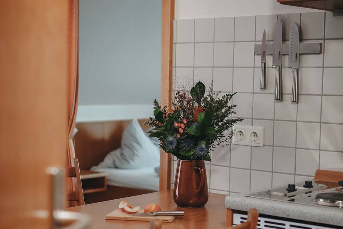 Una cucina con mobili in legno, un tavolo da pranzo con sedie, un vaso con fiori e un quadro appeso al muro.